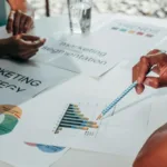 Tim bisnis menganalisis grafik data pelanggan dan strategi pemasaran dalam rapat kerja